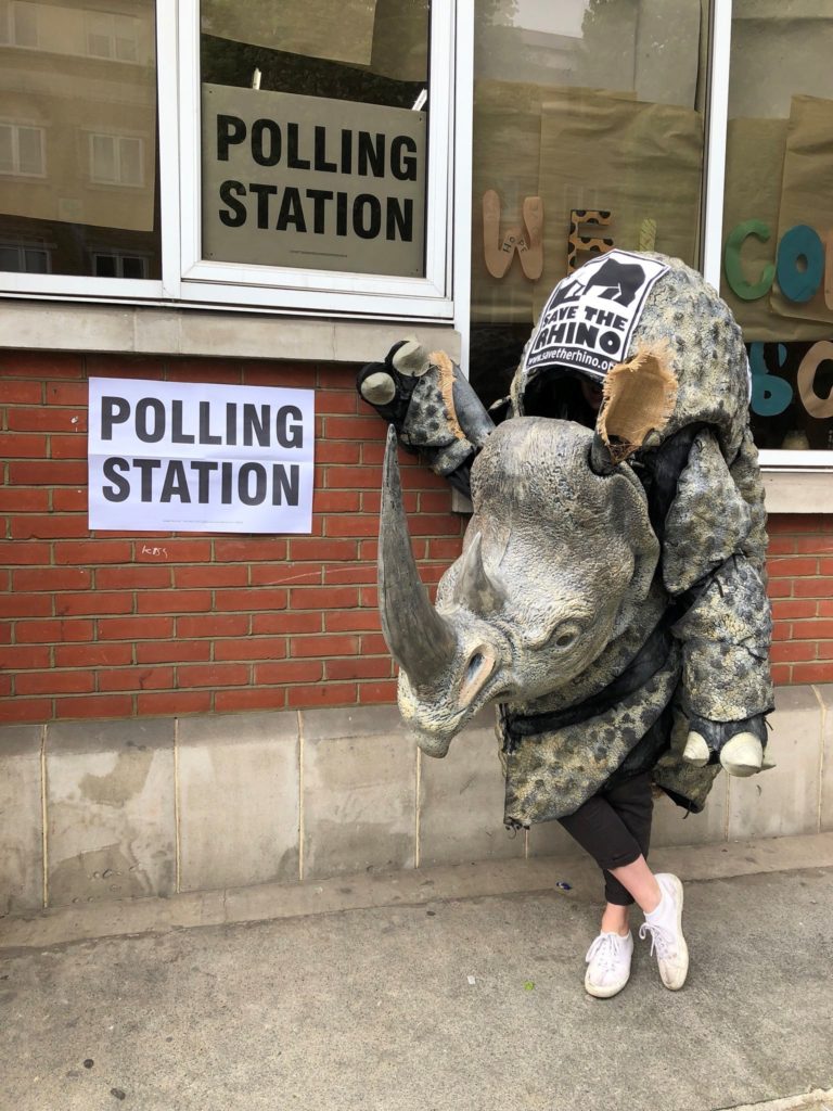 Photo of a rhino costume standing next to a polling station.