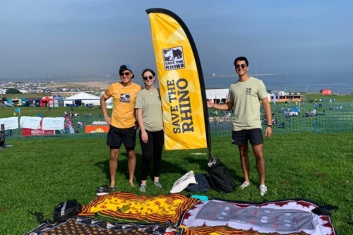 Three people smiling next to a Save the Rhino flag outside.