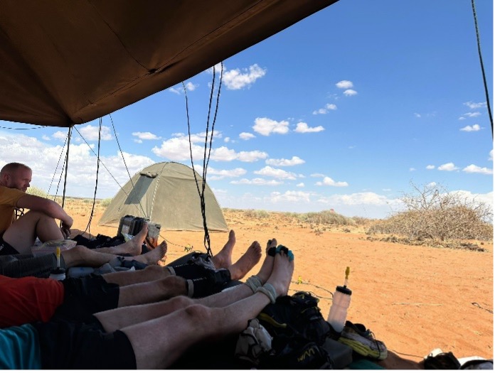 People lying down with their feet up in a tent in the desert.