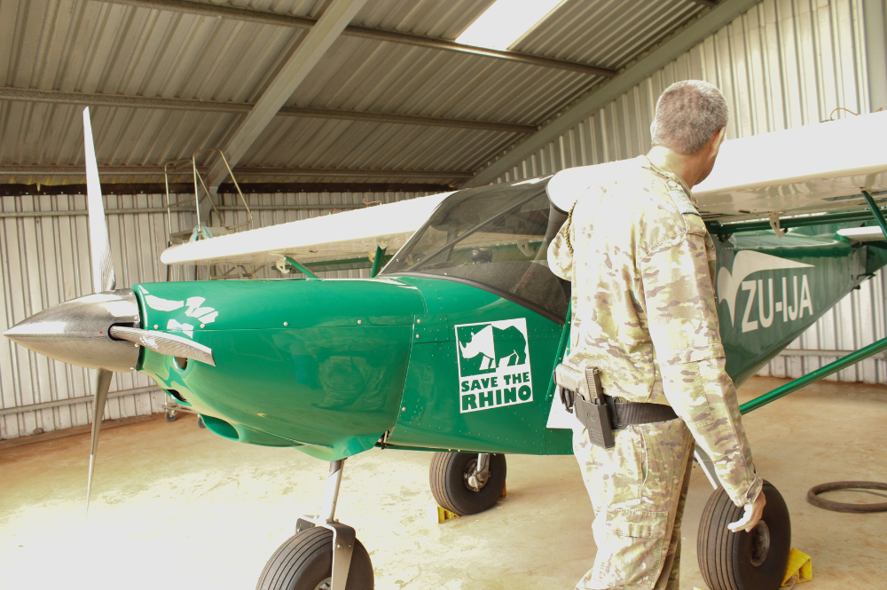 Ranger walking to the side of a small green plane with a Save the Rhino logo on it.