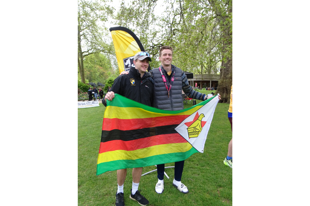 Two people holding a Zimbabwe flag in a park.