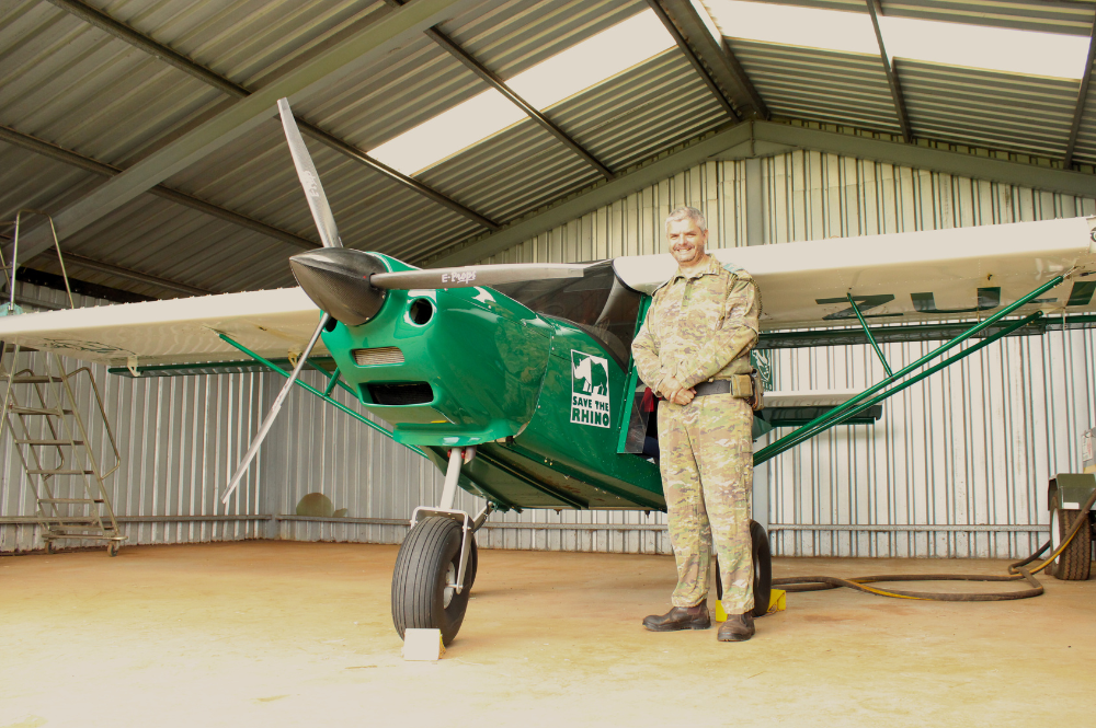 A man in camouflaged uniform standing next to a small green aircraft.