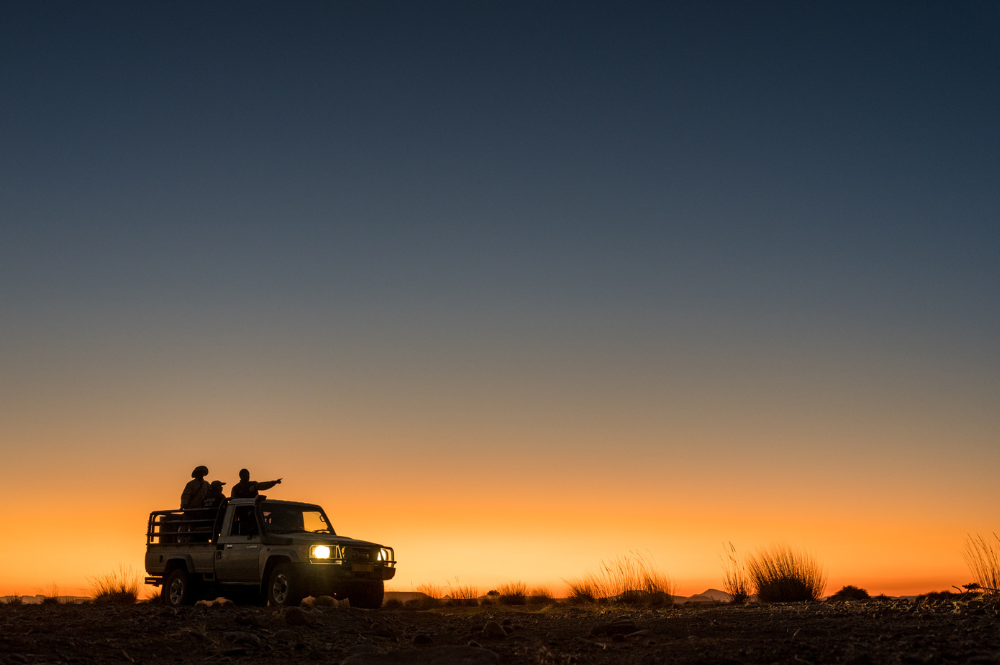 People pointing ahead from a vehicle, driving at sunset.