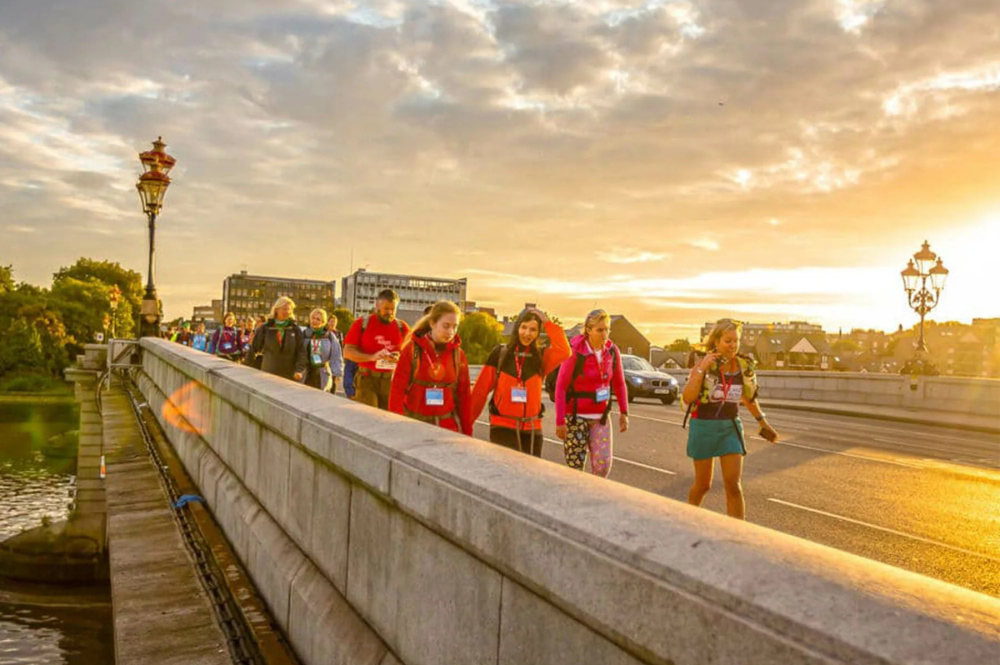 Walkers crossing the Thames Bridge with a sunset in the background