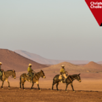 Three people riding mules across a desert. Logo: The Big Give Christmas Challenge