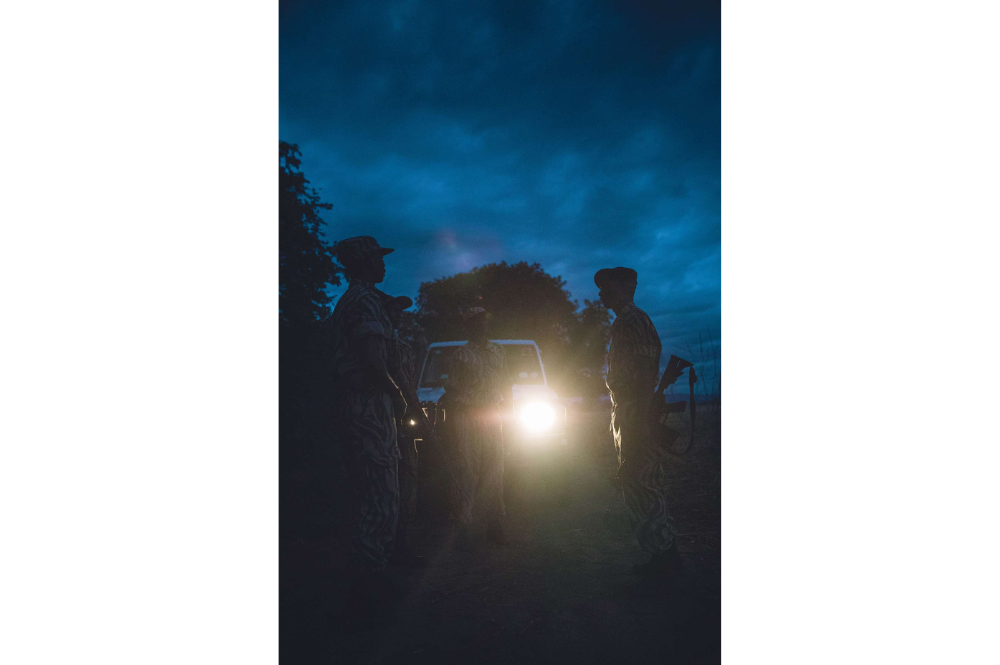 Rangers talking in front of a car in the darkness. Car lights shining through.