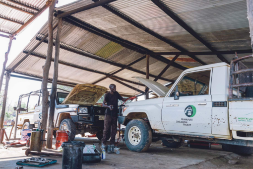 A mechanic fixing two cars in a workshop outside.